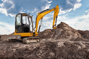 Mini excavator is digging and moving earth at a construction site with a large dirt pile nearby,...