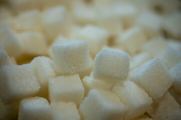 Macro close-up of refined white sugar cubes heap. Sweet crystal texture background. Unhealthy eating, diabetes and calories concept. High sugar consumption symbol