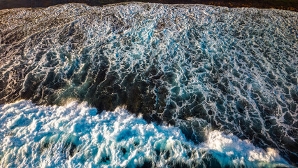 Aerial view of powerful ocean waves crashing against rocky coastline creating white foam patterns on deep blue water surface