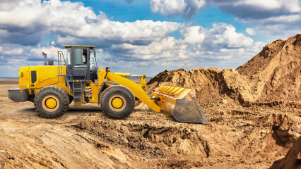Obraz premium A large yellow wheeled bulldozer or loader moves a pile of dirt at a construction site under a cloudy sky, showcasing the activity of land clearing and preparation