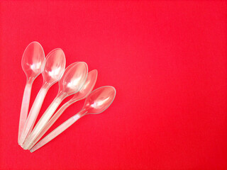 Transparent plastic disposable spoons aligned on red background with copy space. Environmental...
