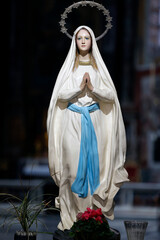 Basilica Santa Maria in Montesanto. Statue of Immaculate Virgin Mary, hands together in prayer, surrounded by flowers .