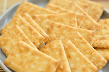 A close-up shot of several rectangular, light brown crackers stacked neatly on a speckled gray plate.