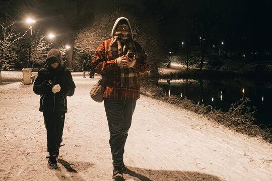 African American man and child walking on snowy path at night, surrounded by trees and lights, enjoying winter evening stroll in a serene park atmosphere