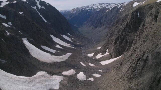 High valley framed by cliffs shows patches of snow nestled between rocks, creating contrasting light zones.