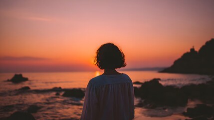 Rear view of a lone person watching the beautiful orange sunset over the sea.