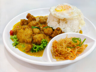 Sizzling chicken curry with steamed rice, fried egg, and side dishes on a white plate delight.