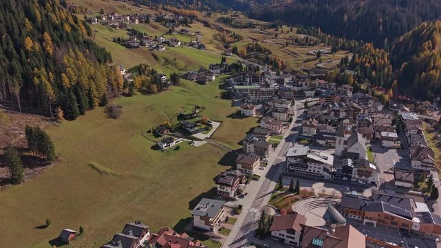 Drone shot of Corvara nestled in golden autumn valley, Dolomites, Italy
