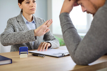 Job interview rejection during business documents and employees resume review on meeting in office. Female recruiter showing denial gesture to male candidate sitting at desk with stress and despair