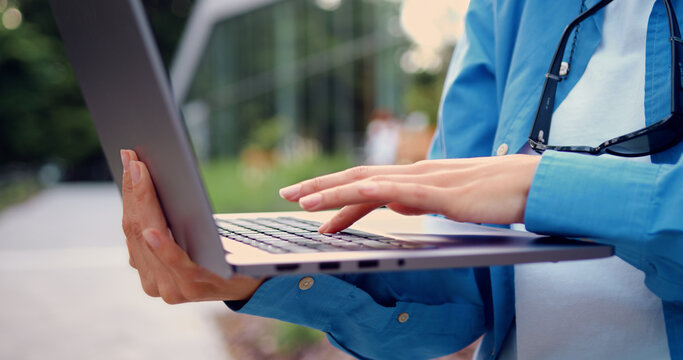 Close-up of female hands typing on a laptop outdoors, working and communicating online. Technology and remote work concept