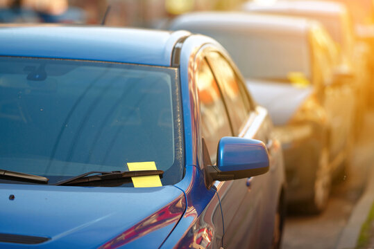 Violation parking ticket on car windshield. Yellow payment notice for parking penalty secured under car's windshield wiper, enforcement of parking laws and the cost of parking violations.