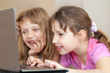 Close-up portrait of two young girls using a laptop indoors, focused and engaged while looking at the screen.