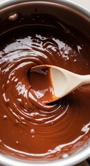 Stirring rich melted chocolate sauce in a metal pot with a wooden spoon
