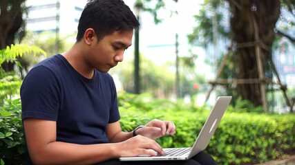 Focused young entrepreneur working on laptop in the park, remote work and digital lifestyle - Powered by Adobe