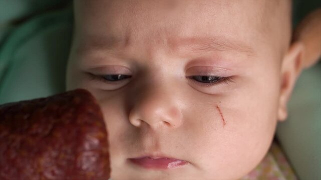 Close-up of a child's face. For the first time, a small baby is given a sniff of complementary foods, a stick of sausage. Blue eyesDay. Flat. Static camera