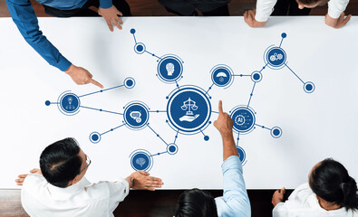 A diverse team engages in a discussion about ethics and justice, highlighted by scales on a table. The surrounding icons symbolize technology and innovation. Amity
