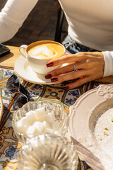 Cappuccino coffee with a heart pattern on the foam in the hands of a girl at a cafe table