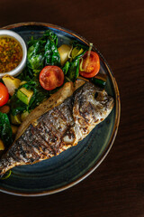 Grilled dorado fish served with vegetables and herbs with lemon on a plate on a wooden table