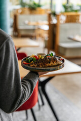 A waiter serves a customer dorado fish with vegetables in a restaurant. Close-up photo