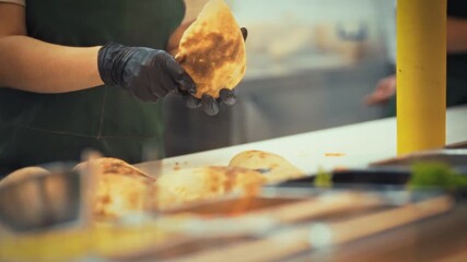 A chef is skillfully preparing pita bun snacks filled with fresh meat and vegetables in a fast food restaurant. The scene captures the quick and efficient atmosphere of food preparation - Powered by Adobe