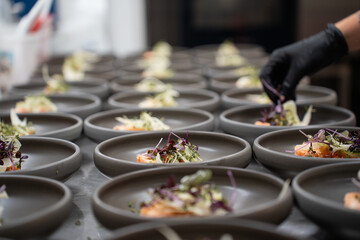 Professional kitchen staff meticulously plate dozens of gourmet appetizers, adding delicate microgreens and herbs for an upscale catering event.