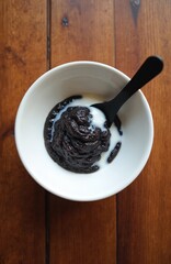 Warm black sticky rice porridge in white bowl on wood table. Creamy coconut milk poured on top, ready to eat with black spoon. Traditional sweet dessert, healthy vegan food for breakfast or any meal.