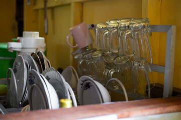 Clear glassware arranged in a drying rack in a bright yellow kitchen. The dishwasher rack filled with sparkling clean plates and glassware in traditional kitchen