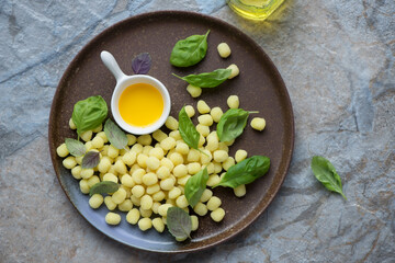 Brown plate with raw italian mini potato gnocchi, horizontal shot on a beige and blue stone background, above view