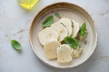 Bowl with fresh halloumi slices and herbs on a light-beige marble background, horizontal shot, high angle view