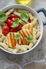 Fusilli pasta with slices of grilled halloumi cheese and roasted tomatoes, vertical shot on a beige granite surface, middle closeup