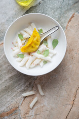 Bowl with cream tteokbokki or rice cakes and steamed dumpling, vertical shot on a grey and roseate granite background, view from above