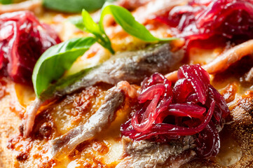 Close-up of fresh, hot pizza topped with anchovies, red onions, melted cheese, and green basil leaves, emphasizing savory texture
