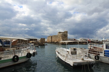 Obraz premium White tour boats docked at historic stone harbor near ancient fortress under dramatic cloudy sky.