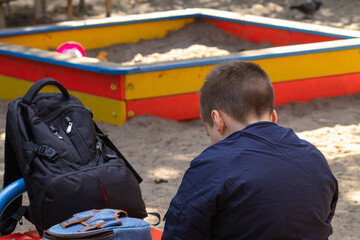 Boy sits on a bench with backpacks on a playground