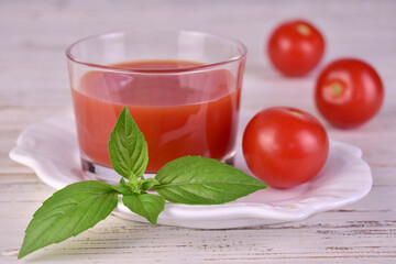 A glass of fresh tomato juice and basil leaf on a white background. Close-up.

