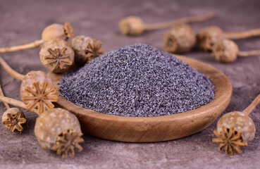 Poppy seeds and poppy heads in a wooden bowl on a gray background. Close-up.
