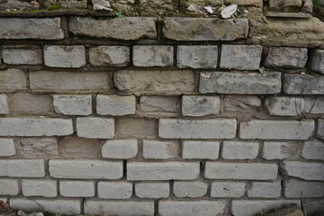 A light gray wall, an old building, a fence with green moss and moisture. Light gray, red bricks, beautiful, stylish brickwork.