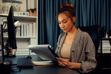Businesswoman focusing on paperwork folder file on working desk, analyzing market planning database website social media online comparing on computer at over late night at modern office. Infobahn.