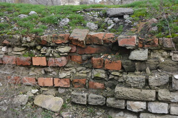 A light gray wall, an old building, a fence with green moss and moisture. Light gray, red bricks, beautiful, stylish brickwork.