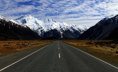 Fototapeta premium Scenic Road Leading to Snow-Capped Mountains Under Cloudy Sky