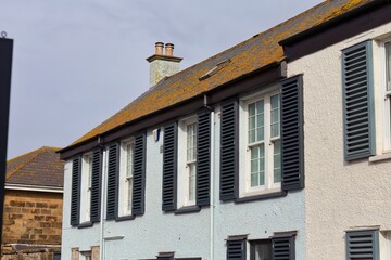 Row of narrow, colorful houses. These whitewashed homes have symmetrical windows with black shutters in Newquay - Cornwall - UK