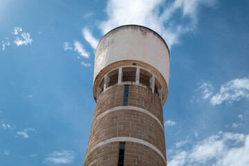 Torre de &aacute;gua hist&oacute;rica de formato cil&iacute;ndrico, revestida a pedra e cimento, destacando-se contra um c&eacute;u azul e algumas nuvens esparsas em Portugal