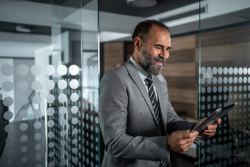 Mature businessman smiling while using digital tablet in office