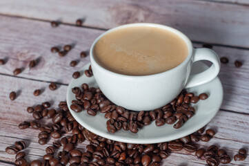 A coffee cup with a white saucer stands on a wooden table with a pile of coffee.