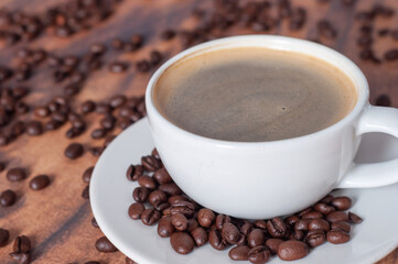 A white coffee cup with black coffee stands on a wooden table with a bunch of