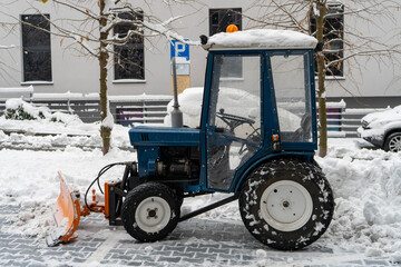Snow-covered compact tractor used for winter street cleaning, urban utility vehicle for snow removal and seasonal maintenance on a snowy residential street