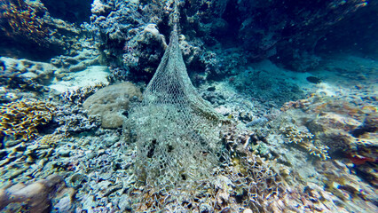 A discarded fishing net lies draped across a damaged coral reef. The abandoned mesh traps debris and highlights the harsh impact of marine pollution underwater. © Houston