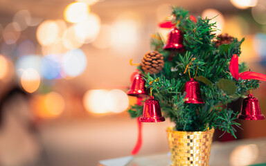 Christmas tree decoration on a table. Small pine tree with shiny red bells, natural pine cones, golden pot. Festive holiday cheer, celebration,winter atmosphere. Beautiful bokeh soft focus background.