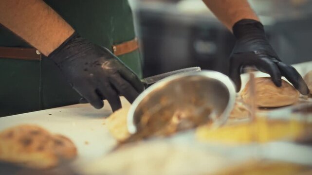 Two chefs in gloves cut a loaf of bread to make pita snacks. This action takes place in a lively kitchen where quick snacks are prepared for hungry visitors