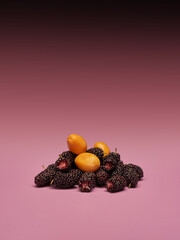 Heap of fresh ripe black mulberries and yellow kumquats isolated on pink background creative food concept